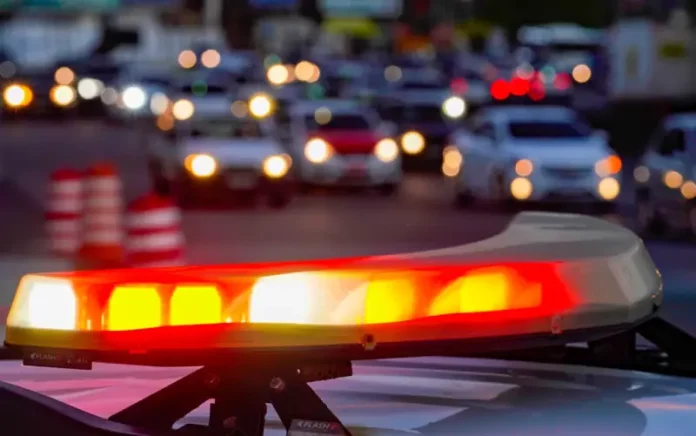 Luzes vermelhas e amarelas de uma viatura policial acesas em primeiro plano, com o trânsito urbano desfocado ao fundo, simbolizando a atuação das forças de segurança no combate aos homicídios e na redução da violência em Santa Catarina.