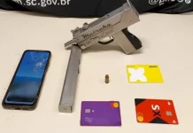 A imagem mostra uma submetralhadora artesanal, um celular e cartões de banco apreendidos durante a operação policial, ilustrando os itens recolhidos pelos agentes.