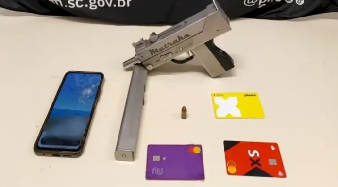 A imagem mostra uma submetralhadora artesanal, um celular e cartões de banco apreendidos durante a operação policial, ilustrando os itens recolhidos pelos agentes.