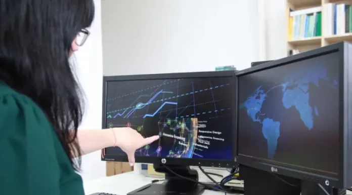 Emprego em Tecnologia da Informação e Comunicação avança 57% em Santa Catarina na última década Mulher trabalhando em frente a dois computadores, apontando para uma tela que exibe gráficos, ilustrando análise de dados e atividades no setor de tecnologia.