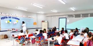 Sala de aula infantil em Florianópolis, com crianças escrevendo em cadernos enquanto a professora escreve no quadro, representando a educação na rede municipal.