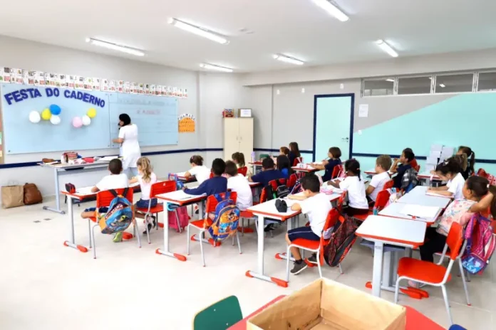 Sala de aula infantil em Florianópolis, com crianças escrevendo em cadernos enquanto a professora escreve no quadro, representando a educação na rede municipal.