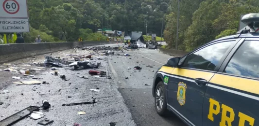 Colisão entre van e carreta na BR-376, entre Santa Catarina e Paraná, deixa um morto e vários feridos. Imagem mostra trecho da BR-376 com destroços espalhados após grave acidente entre van, caminhão e carreta; viatura da Polícia Rodoviária Federal realiza atendimento no local.