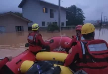 Foto mostra bombeiros em um bote inflável durante operação de resgate em área alagada, ilustrando o trabalho das equipes para alcançar moradores isolados pela enchente em Luiz Alves.
