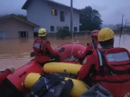 Foto mostra bombeiros em um bote inflável durante operação de resgate em área alagada, ilustrando o trabalho das equipes para alcançar moradores isolados pela enchente em Luiz Alves.