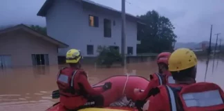 Foto mostra bombeiros em um bote inflável durante operação de resgate em área alagada, ilustrando o trabalho das equipes para alcançar moradores isolados pela enchente em Luiz Alves.
