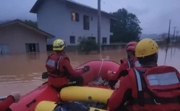 Foto mostra bombeiros em um bote inflável durante operação de resgate em área alagada, ilustrando o trabalho das equipes para alcançar moradores isolados pela enchente em Luiz Alves.