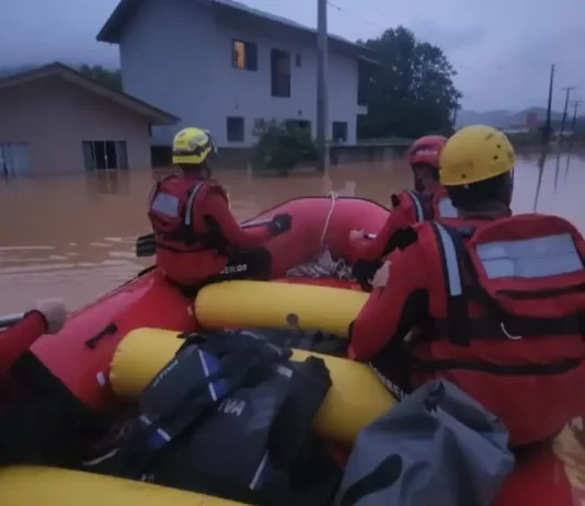 Foto mostra bombeiros em um bote inflável durante operação de resgate em área alagada, ilustrando o trabalho das equipes para alcançar moradores isolados pela enchente em Luiz Alves.