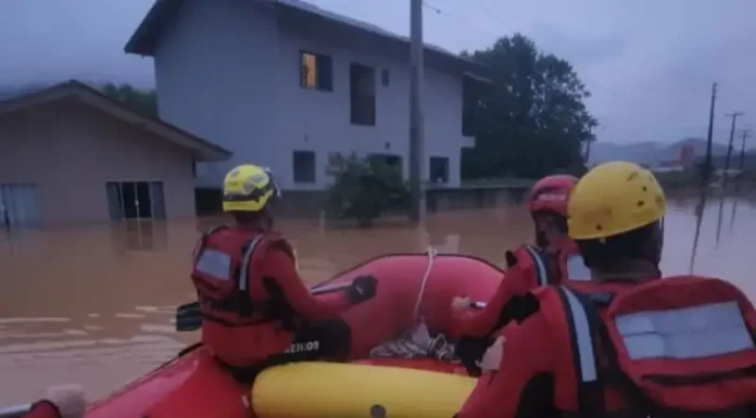 Foto mostra bombeiros em um bote inflável durante operação de resgate em área alagada, ilustrando o trabalho das equipes para alcançar moradores isolados pela enchente em Luiz Alves.
