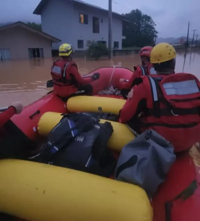 Foto mostra bombeiros em um bote inflável durante operação de resgate em área alagada, ilustrando o trabalho das equipes para alcançar moradores isolados pela enchente em Luiz Alves.