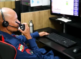 Bombeiro do CBMSC trabalha no computador enquanto fala no rádio para ilustrar o uso de tecnologias que apoiam o atendimento às ocorrências.