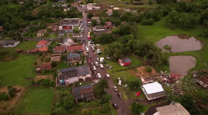 Vista aérea mostra parte de Dionísio Cerqueira após a passagem de tornados, com casas destelhadas, destroços espalhados e equipes atuando nas ruas para avaliar os danos e prestar atendimento à população. A imagem ilustra a dimensão dos estragos causados pelo fenômeno climático.