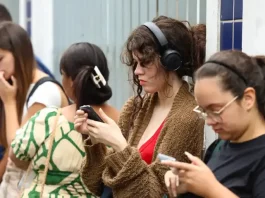 Candidatas conferem informações no celular enquanto aguardam a abertura dos portões para participar do Enem.