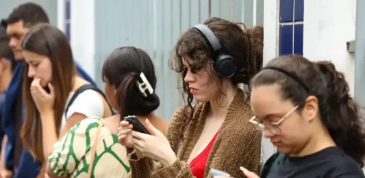 Enem 2025: prazo para pedir reaplicação termina na sexta-feira (21) Candidatas conferem informações no celular enquanto aguardam a abertura dos portões para participar do Enem.