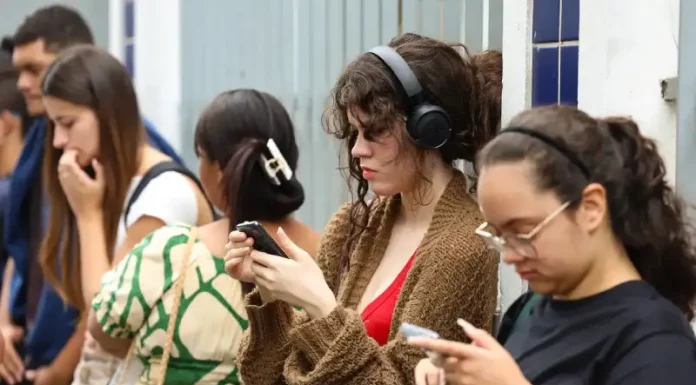 Candidatas conferem informações no celular enquanto aguardam a abertura dos portões para participar do Enem.