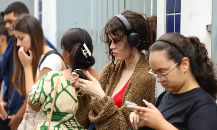 Candidatas conferem informações no celular enquanto aguardam a abertura dos portões para participar do Enem.