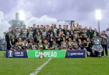 Imagem do elenco e comissão técnica do Figueirense reunidos no gramado do Estádio Orlando Scarpelli para registrar a celebração do título da Copa SC, destacando o troféu ao centro e a faixa de campeão exibida na frente do grupo.