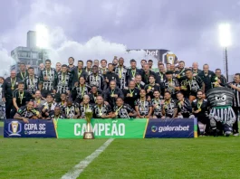 Figueirense é campeão da Copa SC; Criciúma tropeça e Chapecoense volta à Série A Imagem do elenco e comissão técnica do Figueirense reunidos no gramado do Estádio Orlando Scarpelli para registrar a celebração do título da Copa SC, destacando o troféu ao centro e a faixa de campeão exibida na frente do grupo.