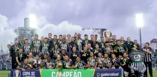 Imagem do elenco e comissão técnica do Figueirense reunidos no gramado do Estádio Orlando Scarpelli para registrar a celebração do título da Copa SC, destacando o troféu ao centro e a faixa de campeão exibida na frente do grupo.