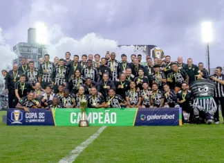 Imagem do elenco e comissão técnica do Figueirense reunidos no gramado do Estádio Orlando Scarpelli para registrar a celebração do título da Copa SC, destacando o troféu ao centro e a faixa de campeão exibida na frente do grupo.