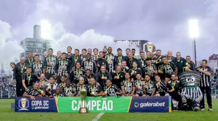 Imagem do elenco e comissão técnica do Figueirense reunidos no gramado do Estádio Orlando Scarpelli para registrar a celebração do título da Copa SC, destacando o troféu ao centro e a faixa de campeão exibida na frente do grupo.