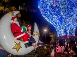 São José lança o Natal Iluminado e estreia a Vila Mágica do Natal Luzes da Esperança A imagem mostra uma cena natalina usada para divulgar o Natal Iluminado de São José. Um Papai Noel decorativo está sentado em uma lua gigante ao lado de uma criança, enquanto ao fundo aparece uma grande estrutura iluminada em azul em formato de balão e famílias aproveitam o espaço. A foto reforça o clima festivo e a proposta de oferecer atrações para as famílias durante o evento.