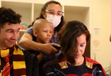 Criança paciente com câncer infantil raspando o cabelo de um super-herói, simbolizando solidariedade e a campanha de diagnóstico precoce.