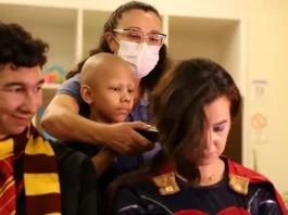 Super-heróis têm cabelo raspado em ação pelo diagnóstico precoce do câncer infantil Criança paciente com câncer infantil raspando o cabelo de um super-herói, simbolizando solidariedade e a campanha de diagnóstico precoce.