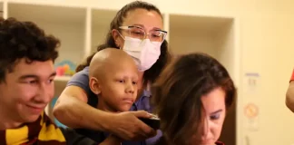 Criança paciente com câncer infantil raspando o cabelo de um super-herói, simbolizando solidariedade e a campanha de diagnóstico precoce.