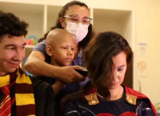Super-heróis têm cabelo raspado em ação pelo diagnóstico precoce do câncer infantil Criança paciente com câncer infantil raspando o cabelo de um super-herói, simbolizando solidariedade e a campanha de diagnóstico precoce.