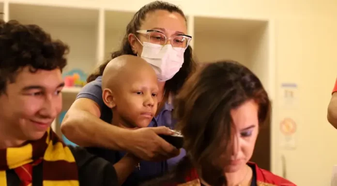 Criança paciente com câncer infantil raspando o cabelo de um super-herói, simbolizando solidariedade e a campanha de diagnóstico precoce.