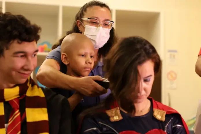 Raspando cabelo HIJG Criança paciente com câncer infantil raspando o cabelo de um super-herói, simbolizando solidariedade e a campanha de diagnóstico precoce.