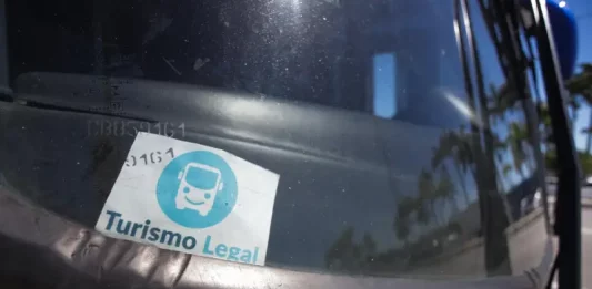 Parabrisa de um veículo de turismo com o Selo Turismo Legal fixado, indicando que o veículo está credenciado para operar conforme as regras da cidade.