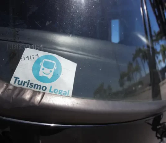 Parabrisa de um veículo de turismo com o Selo Turismo Legal fixado, indicando que o veículo está credenciado para operar conforme as regras da cidade.