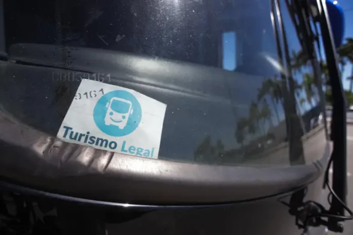 Parabrisa de um veículo de turismo com o Selo Turismo Legal fixado, indicando que o veículo está credenciado para operar conforme as regras da cidade.