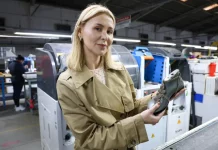 A imagem mostra a empresária Suzana Santos em uma fábrica de calçados, segurando um modelo de sapato para representar a presença e a liderança das mulheres no empreendedorismo catarinense.