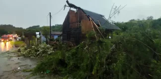 Casa com parte do telhado destruída e árvores caídas após ventos fortes, ilustrando os danos provocados pelo mau tempo em Santa Catarina.