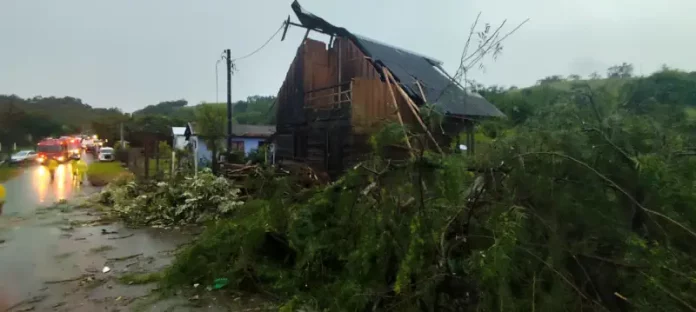 Vento forte Casa com parte do telhado destruída e árvores caídas após ventos fortes, ilustrando os danos provocados pelo mau tempo em Santa Catarina.