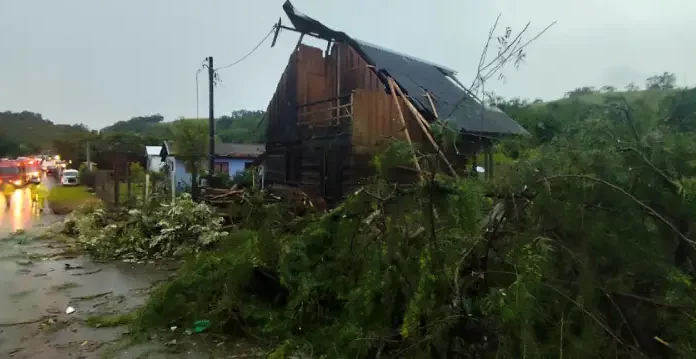 Casa com parte do telhado destruída e árvores caídas após ventos fortes, ilustrando os danos provocados pelo mau tempo em Santa Catarina.