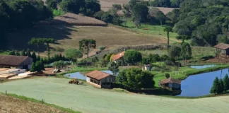 Imagem de uma propriedade rural com casa, açudes e trator em operação, ilustrando os investimentos e a geração de empregos do programa Coopera Agro SC no campo.