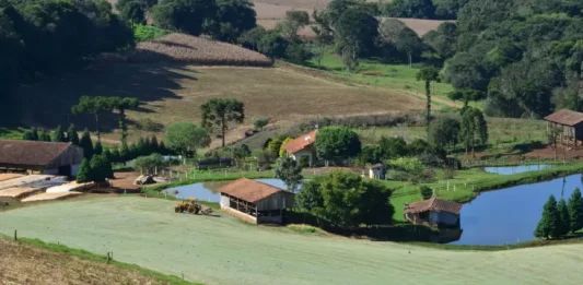Imagem de uma propriedade rural com casa, açudes e trator em operação, ilustrando os investimentos e a geração de empregos do programa Coopera Agro SC no campo.