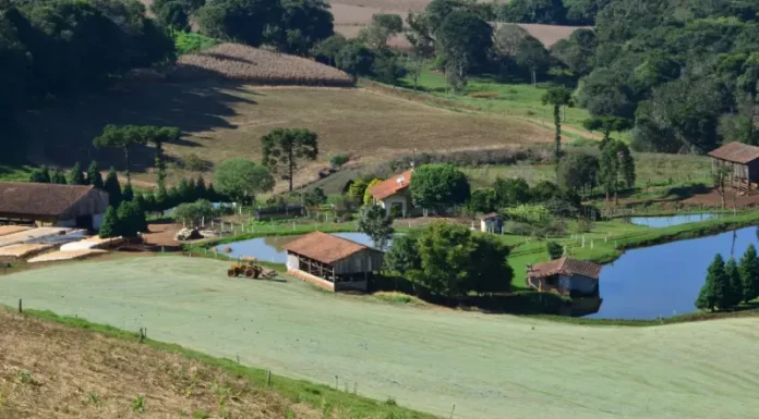 Imagem de uma propriedade rural com casa, açudes e trator em operação, ilustrando os investimentos e a geração de empregos do programa Coopera Agro SC no campo.