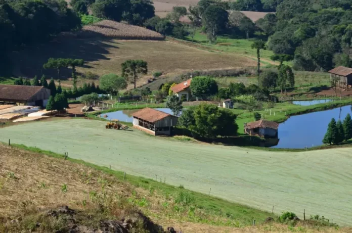 agronegócio (1) Imagem de uma propriedade rural com casa, açudes e trator em operação, ilustrando os investimentos e a geração de empregos do programa Coopera Agro SC no campo.