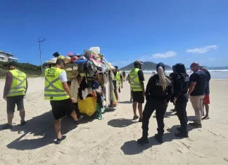 Agentes da Prefeitura e da Polícia Militar abordam um carrinho carregado de produtos irregulares nas praias para ilustrar a fiscalização contra o comércio ambulante ilegal em Florianópolis.