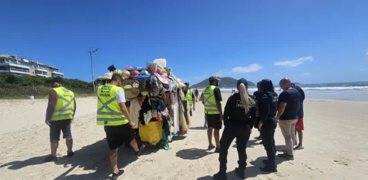 Agentes da Prefeitura e da Polícia Militar abordam um carrinho carregado de produtos irregulares nas praias para ilustrar a fiscalização contra o comércio ambulante ilegal em Florianópolis.
