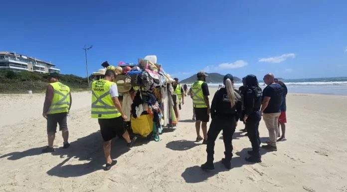 Agentes da Prefeitura e da Polícia Militar abordam um carrinho carregado de produtos irregulares nas praias para ilustrar a fiscalização contra o comércio ambulante ilegal em Florianópolis.