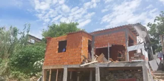 Operários demolindo uma construção irregular em um costão à beira-mar.