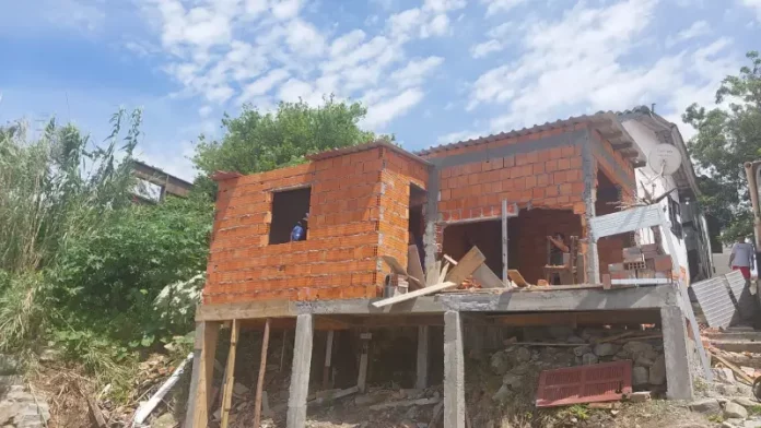 Operários demolindo uma construção irregular em um costão à beira-mar.