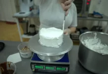 Trabalho e qualificação mudam a rotina de mulheres em unidades prisionais de Santa Catarina Pessoa realiza trabalho de confeitaria ao aplicar cobertura em um bolo na cozinha de uma unidade prisional, durante atividade de capacitação profissional.