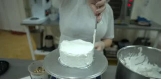 Pessoa realiza trabalho de confeitaria ao aplicar cobertura em um bolo na cozinha de uma unidade prisional, durante atividade de capacitação profissional.